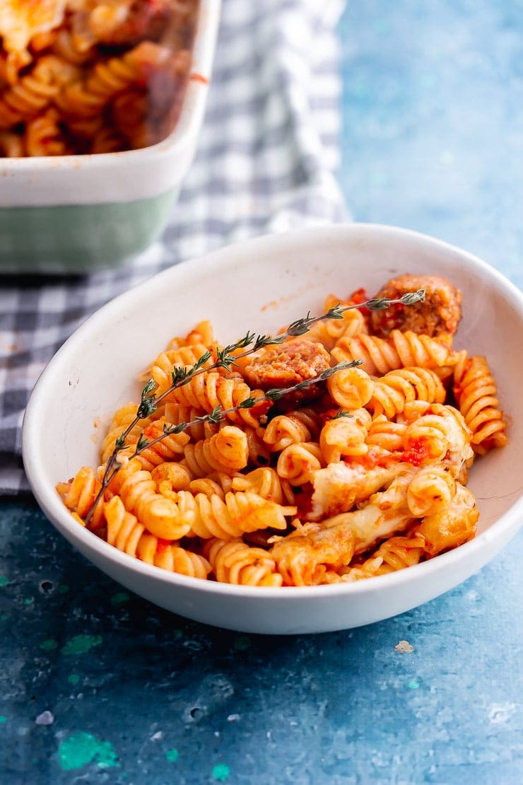 White bowl of veggie sausage pasta bake on a blue background