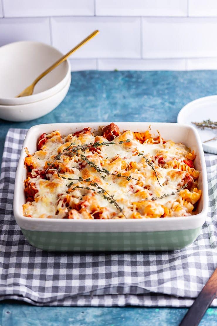 Green baking dish of veggie sausage pasta bake on a blue background