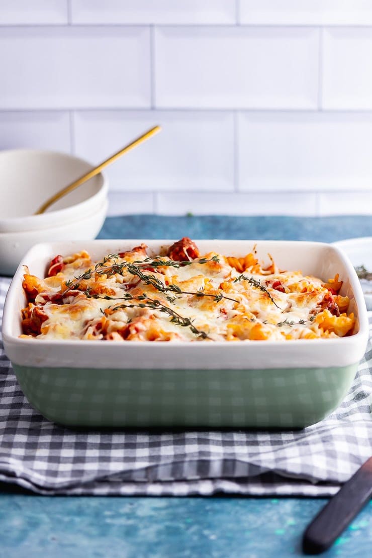 Side on shot of vegetarian sausage pasta bake in a green dish on a checked cloth