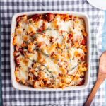 Overhead shot of vegetarian sausage pasta bake on a checked cloth with wooden spoon