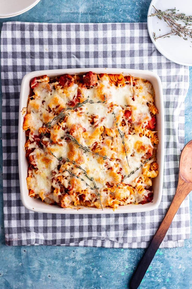 Overhead shot of vegetarian sausage pasta bake on a checked cloth with wooden spoon