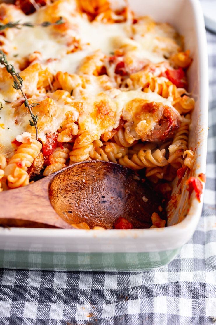 Wooden spoon in a vegetarian sausage pasta bake in a green dish