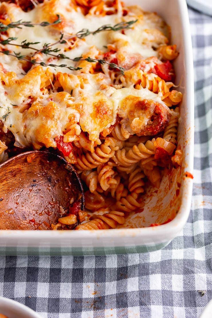 Wooden spoon with a portion take from sausage pasta bake on a checked cloth