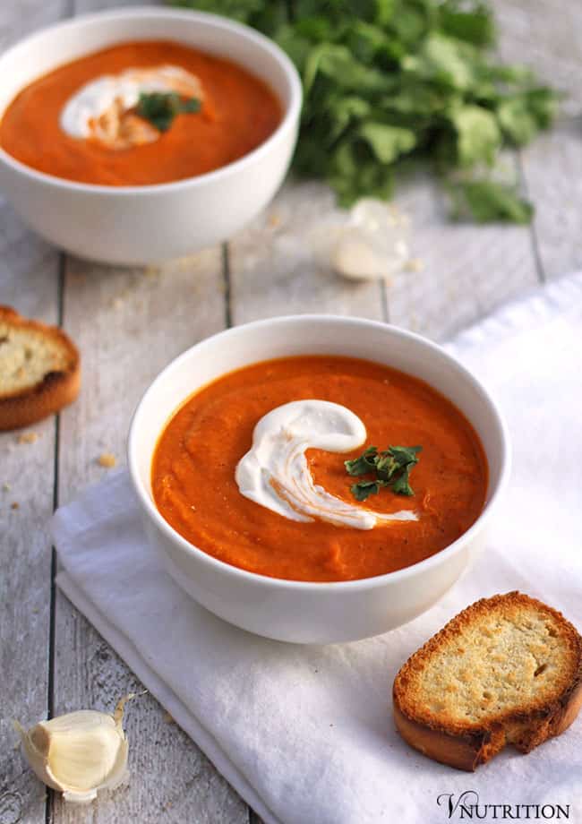 White bowl of tomato and chickpea soup on a white cloth with bread