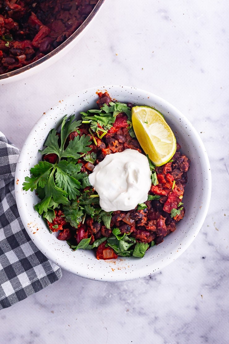 Overhead shot of a white bowl of bean chilli with sour cream and lime