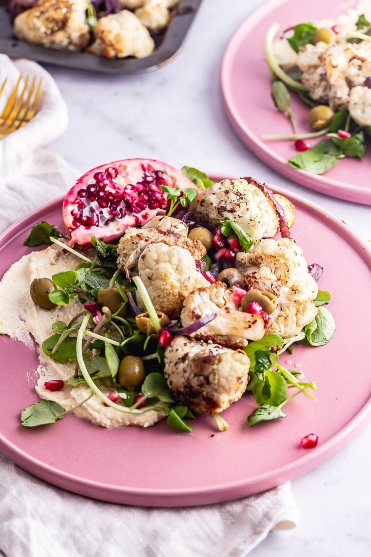 Pink plate of cauliflower salad with pomegranate and greens