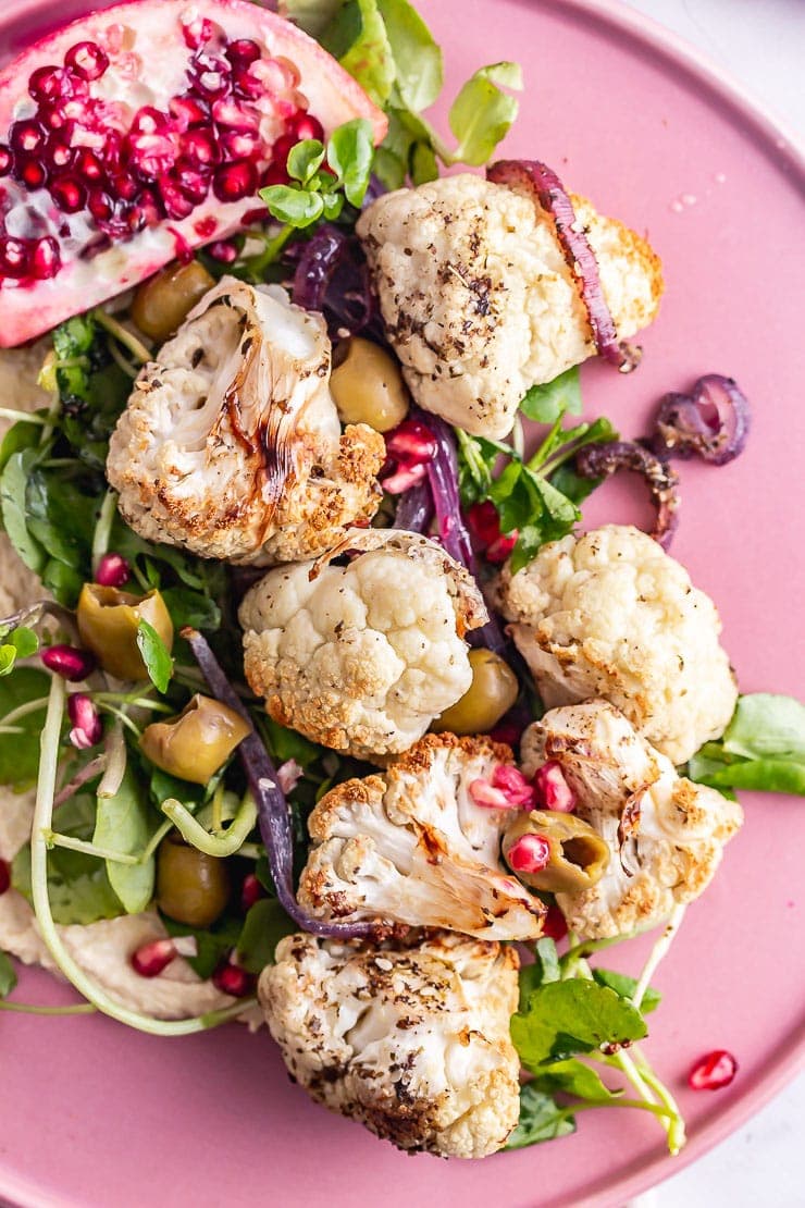 Close up of cauliflower salad with greens on a pink plate