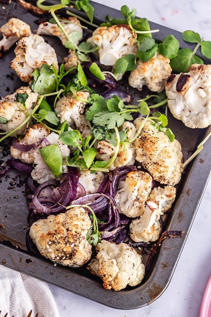 Overhead shot of roasted cauliflower and onions with greens on a baking sheet