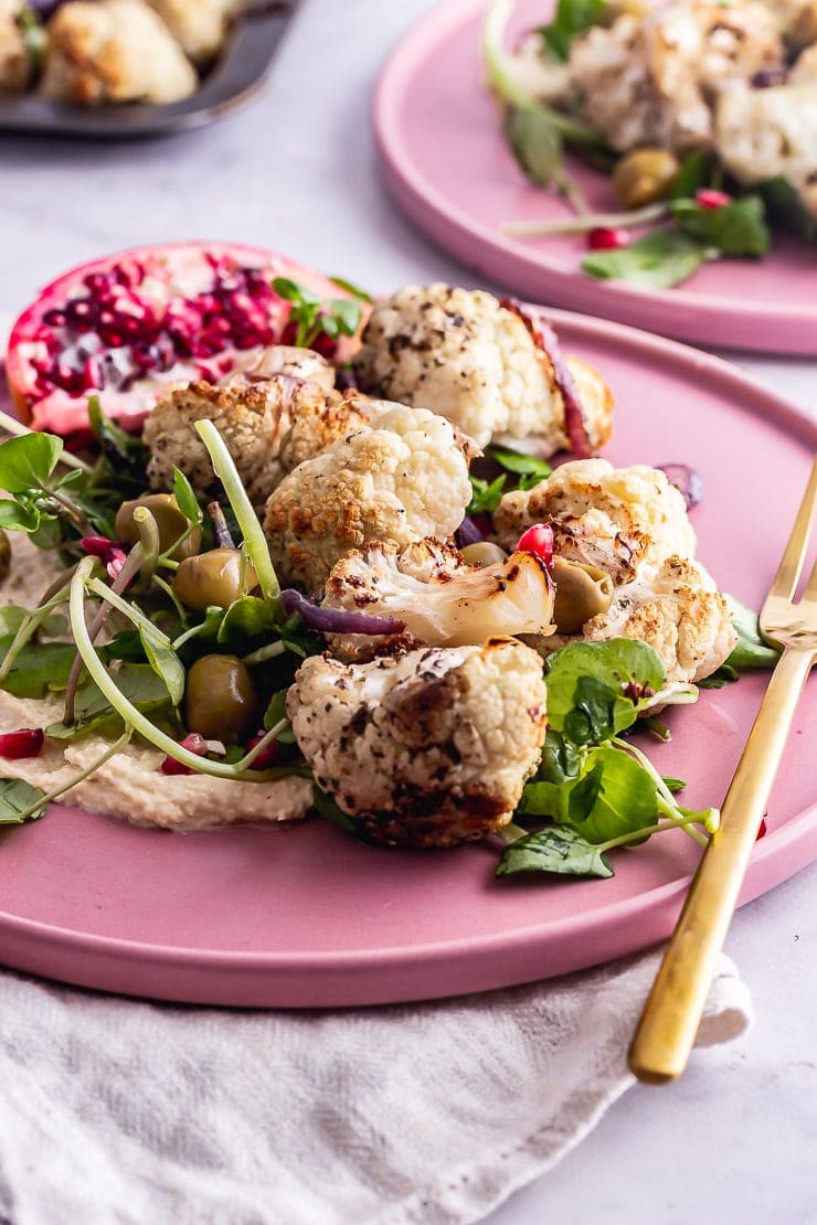 Close up of cauliflower salad on a pink plate with a gold fork