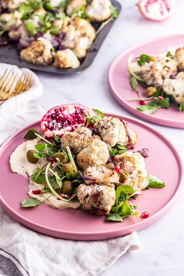 Pink plates of cauliflower salad with hummus and greens on a marble background