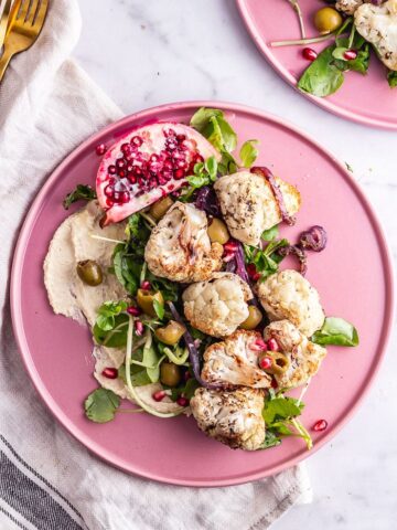 Overhead shot of cauliflower salad on a pink plate on a marble surface