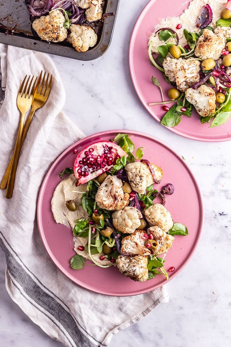 Overhead shot of two plates of cauliflower salad on pink plates with gold forks on a marble background