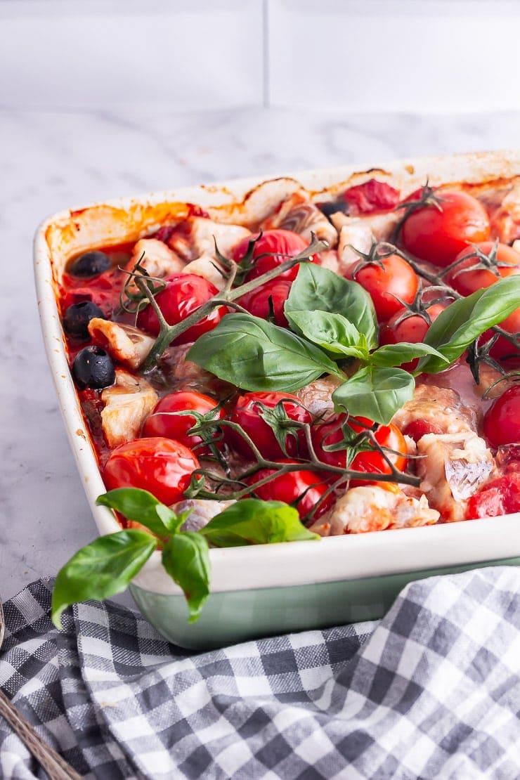 Green baking dish of baked fish and vegetables in tomato sauce with basil