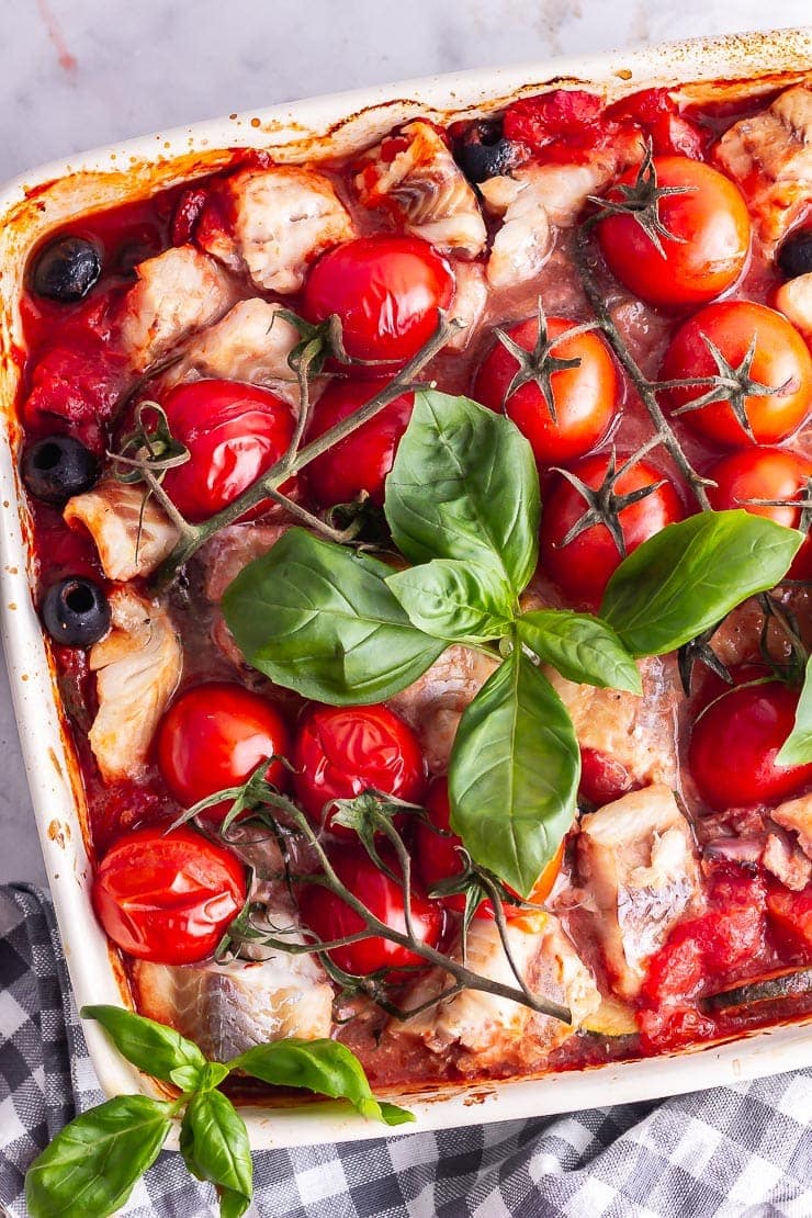 Overhead shot of fish and vegetable bake with basil and a checked cloth