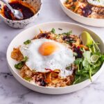 White bowl of kimchi fried rice topped with a fried egg with greens