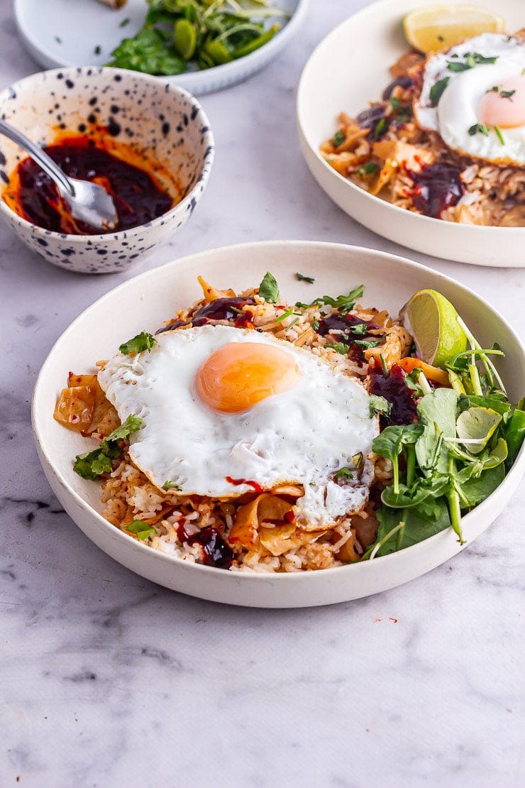 White bowl of kimchi fried rice topped with a fried egg with greens