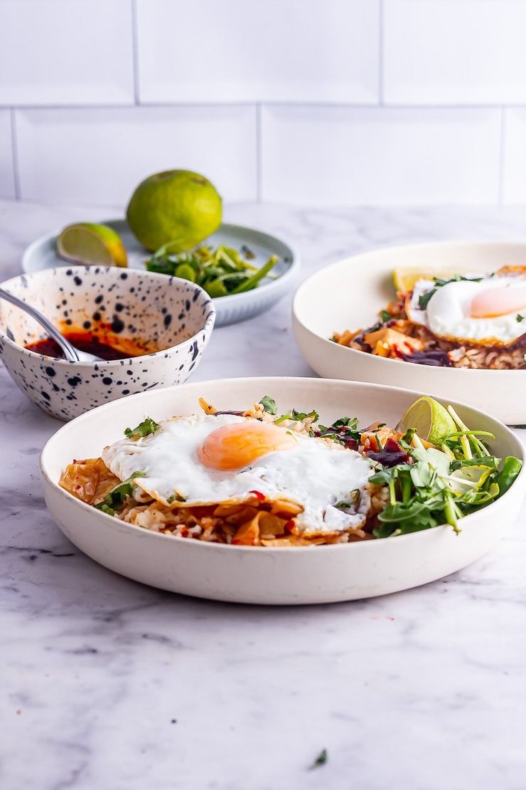 Side on shot of white bowl of kimchi fried rice with a white brick background