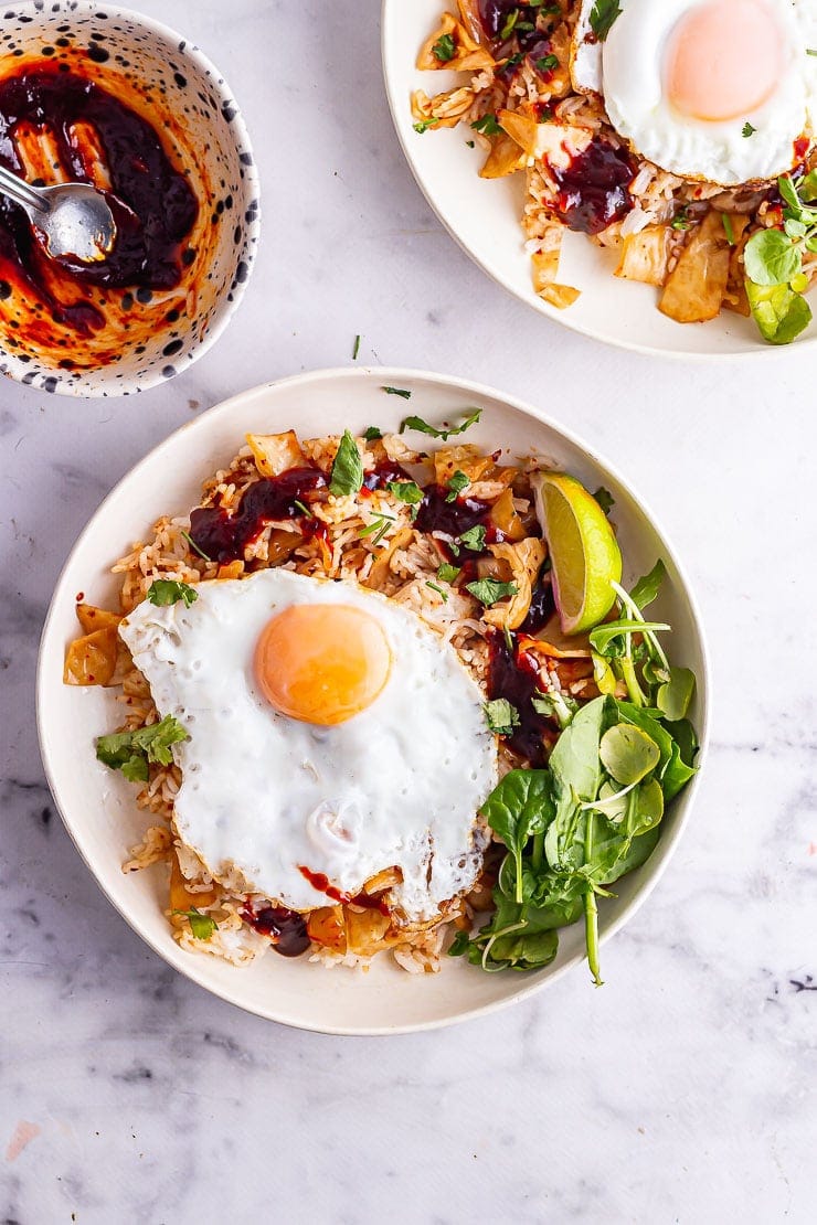 Overhead shot of kimchi fried rice in a cream bowl with greens