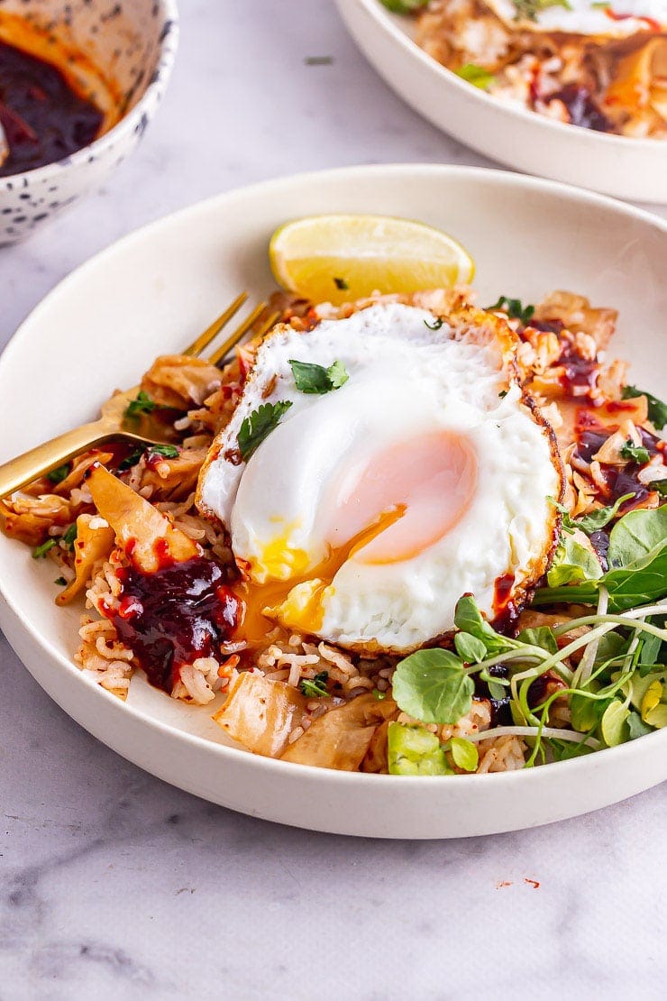 Yolk running on kimchi fried rice with a gold fork and greens