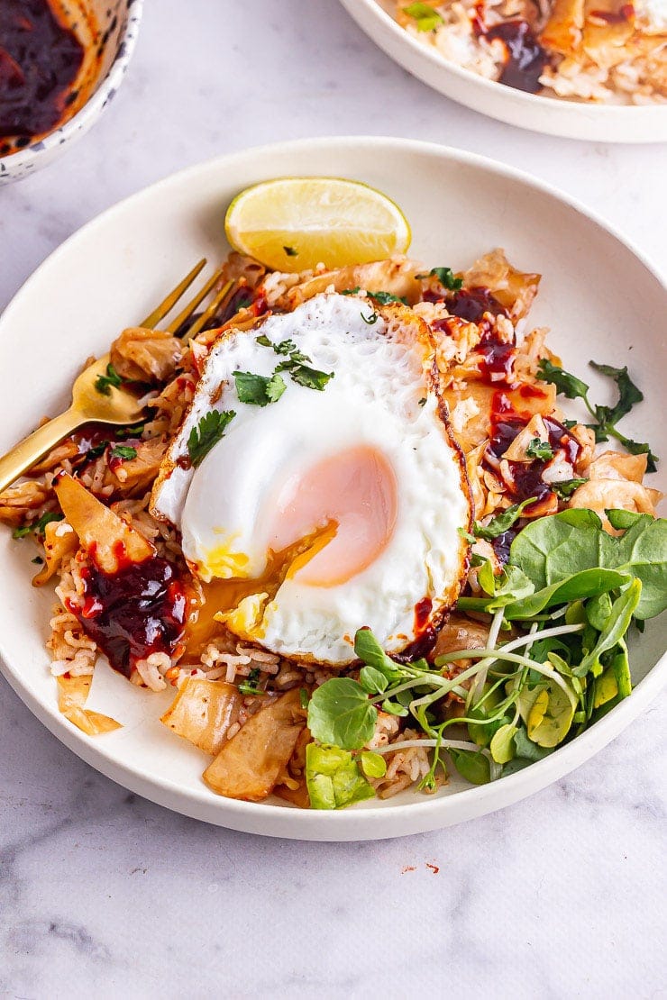 Fried egg dripping yolk onto kimchi fried rice with a gold fork