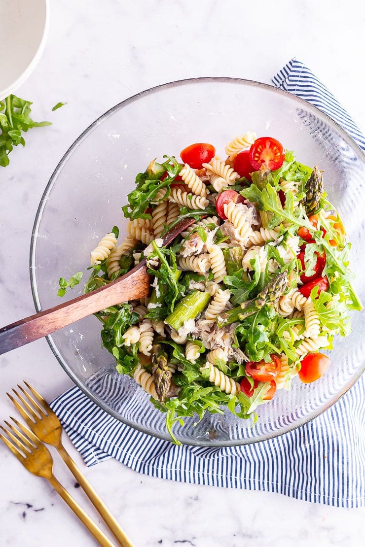 Overhead shot of mackerel pasta salad with a wooden spoon on a striped cloth