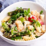 White bowl of mackerel pasta salad with asparagus and cherry tomatoes on a marble surface