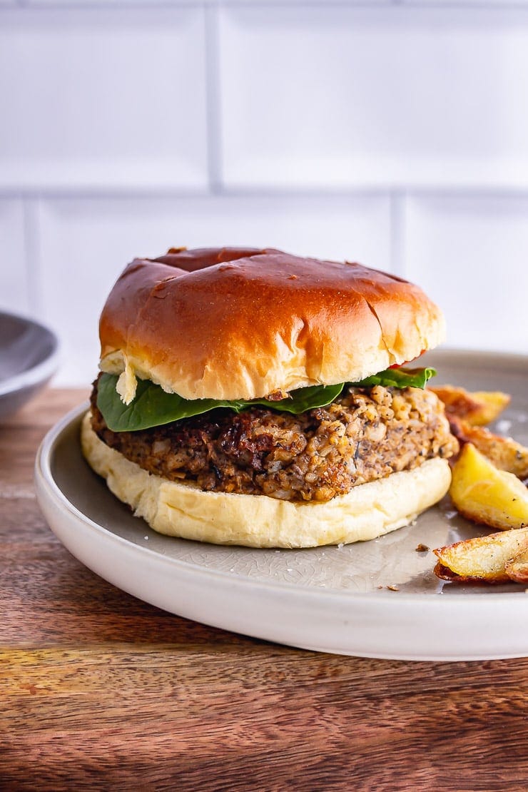 Side on shot of mushroom burger in a bun with chips on a wooden surface