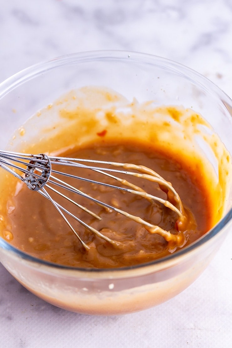 Glass bowl of peanut sesame dressing with whisk