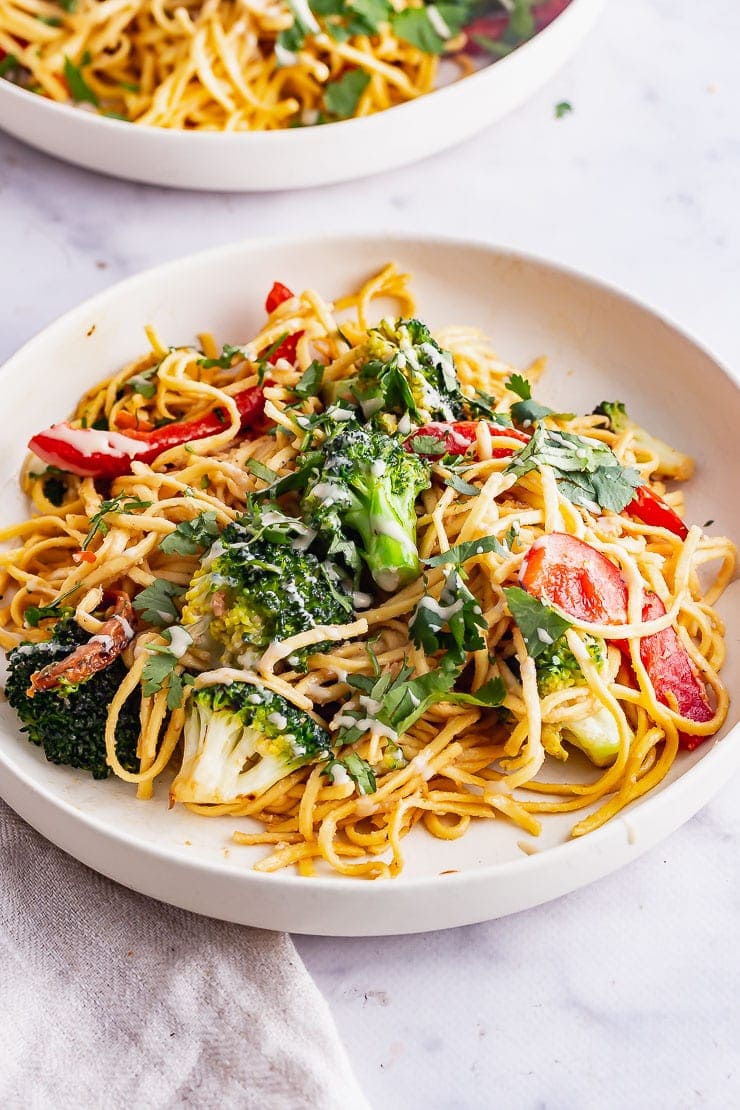 White bowl of noodles with herbs and peppers on a marble surface