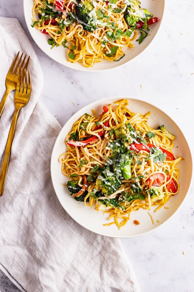 Overhead shot of two bowls of sesame noodle salad with gold forks on a cream cloth