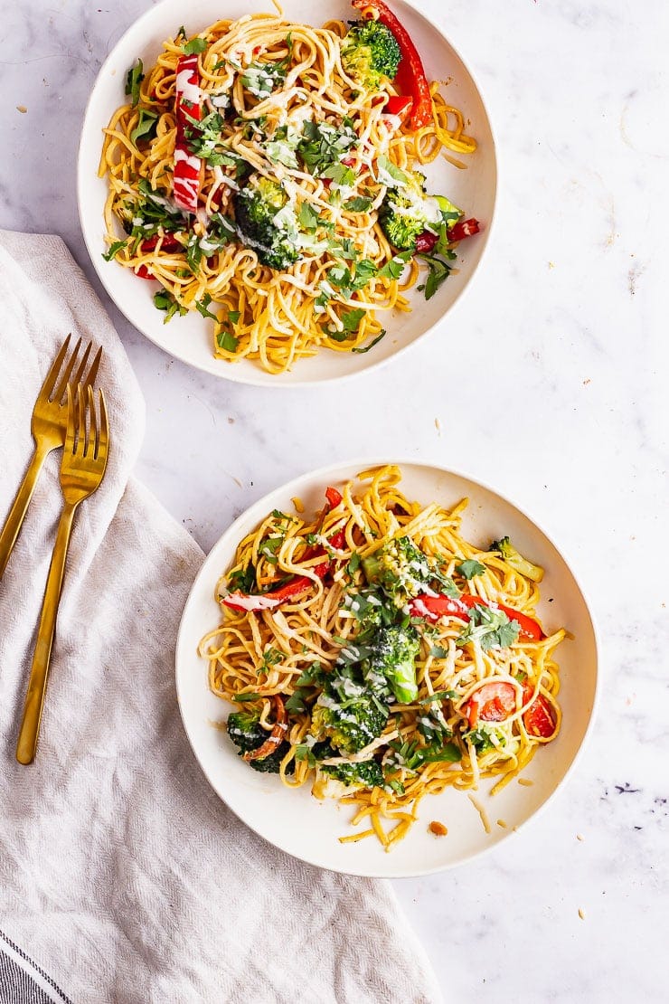 Overhead shot of two bowls of noodle salad with gold forks on a marble background