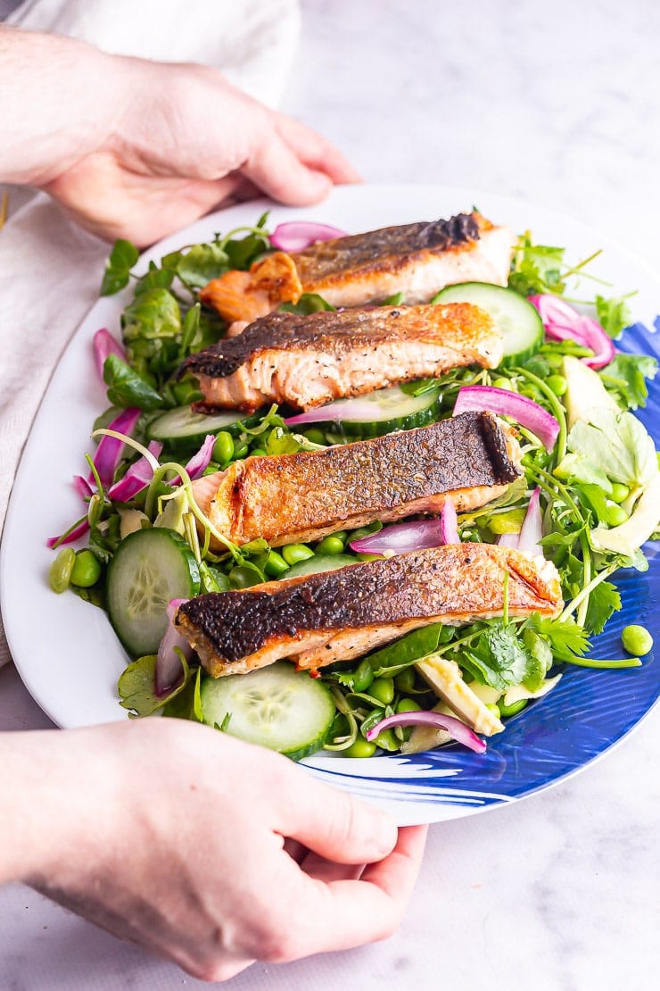 Hands holding a platter of salmon salad on a marble background