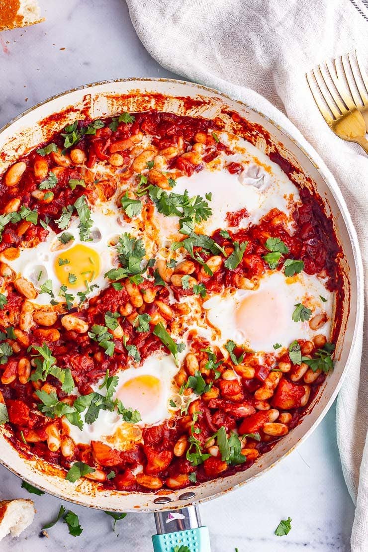 Overhead shot of spicy beans and eggs in a blue skillet on a marble background