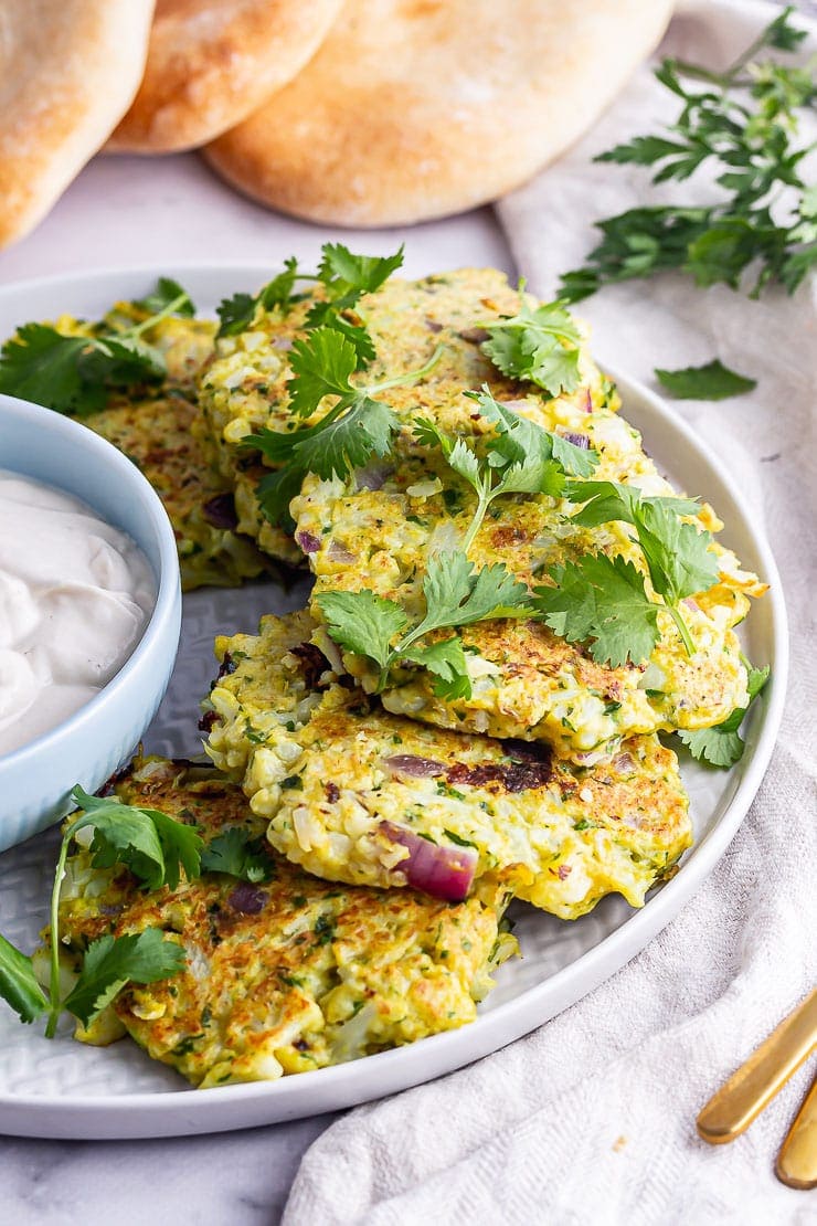 Grey plate of cauliflower fritters with herbs on a marble surface