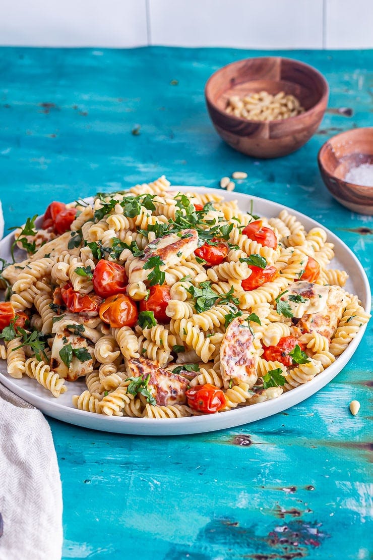 Platter of halloumi pasta with tomatoes on a bright blue background