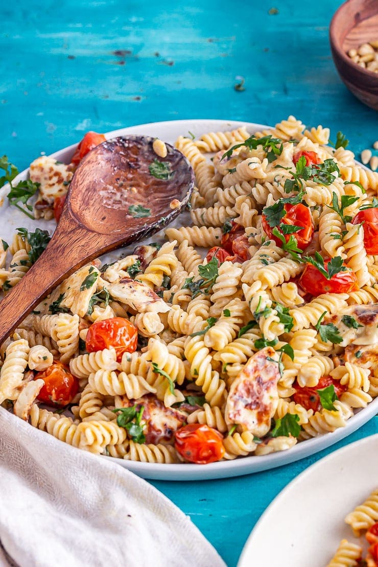 Platter of halloumi pasta with a wooden spoon and a portion taken