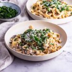 Two bowls of mushroom tagliatelle with parsley on a marble background