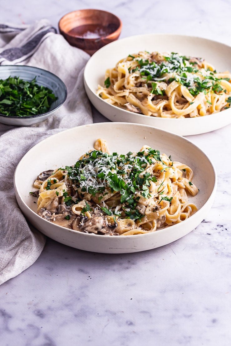 Two bowls of mushroom tagliatelle with parsley on a marble background