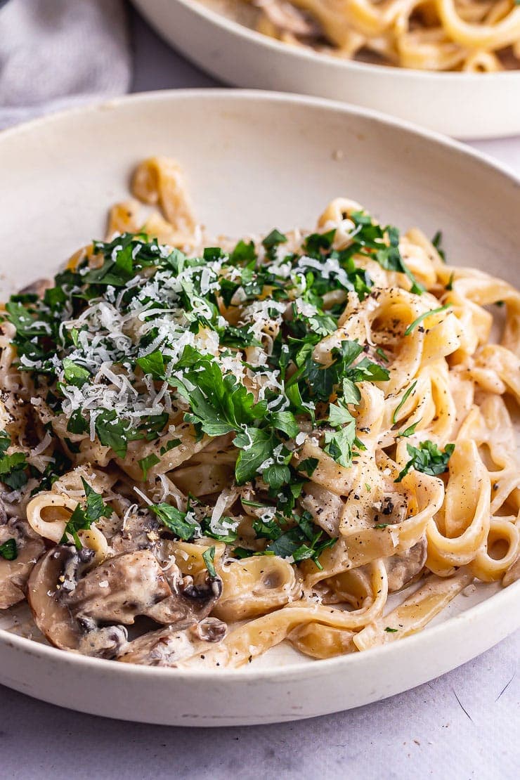 Mushroom tagliatelle topped with parsley and parmesan in a cream bowl