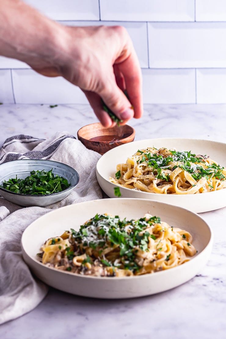 Hand sprinkling herbs over a bowl of mushroom tagliatelle