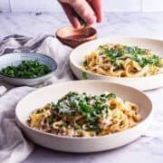 Side shot of mushroom tagliatelle with hand sprinkling herbs