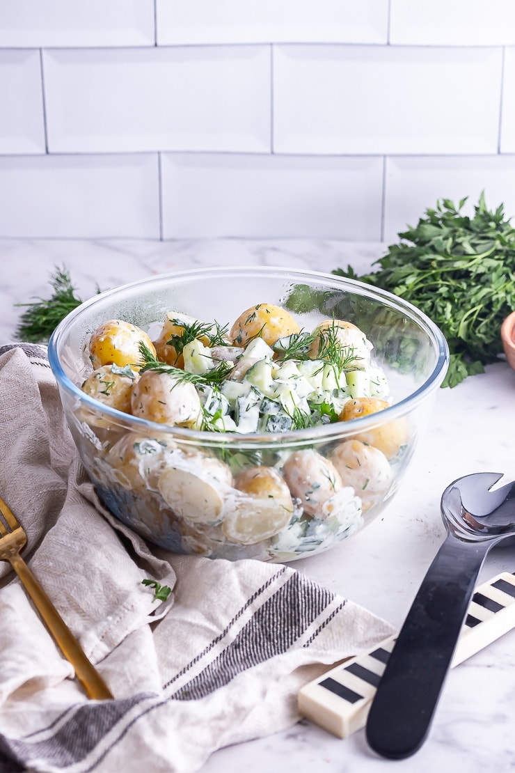 Side on shot of healthy potato salad in front of a white brick wall with herbs in the background