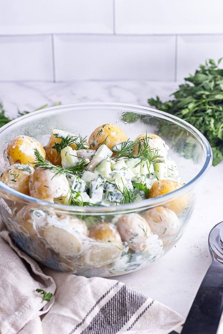 Glass bowl of potato salad with herbs on a marble surface