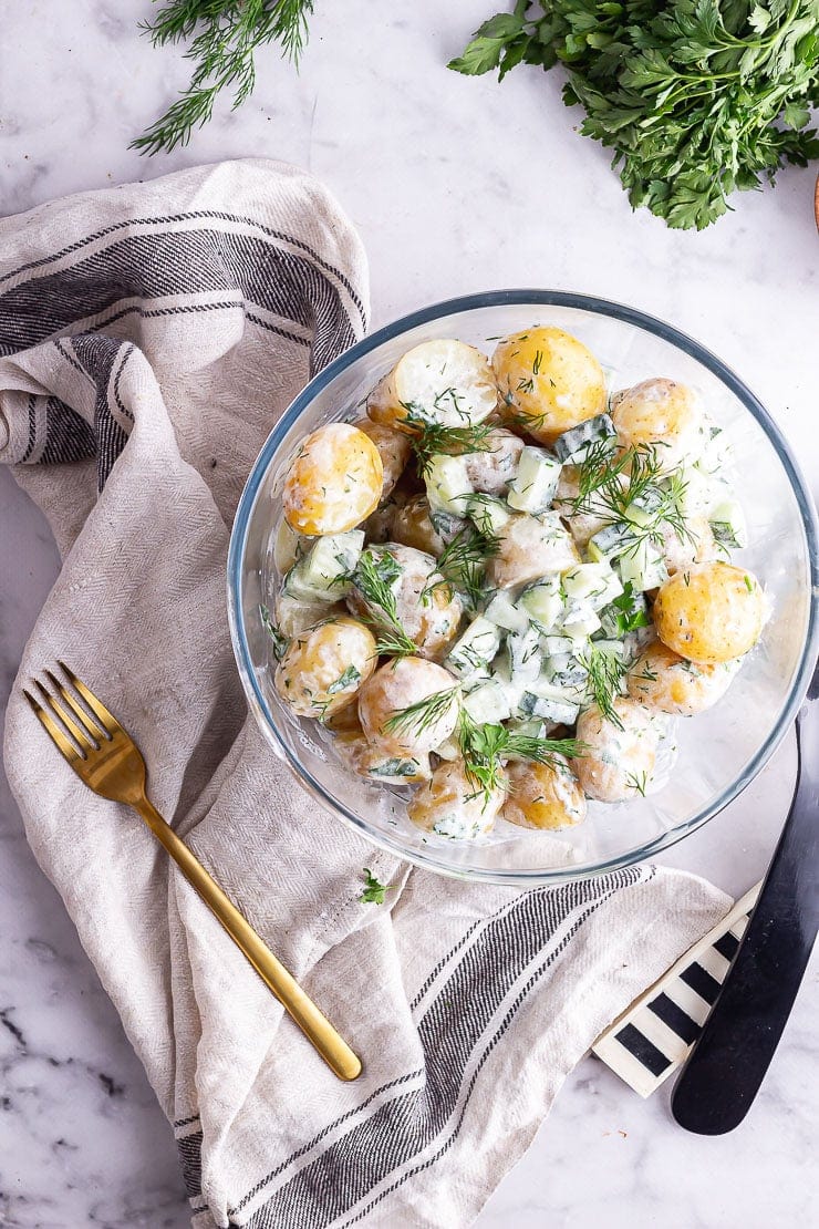 Overhead shot of glass bowl of healthy potato salad with a cloth and herbs