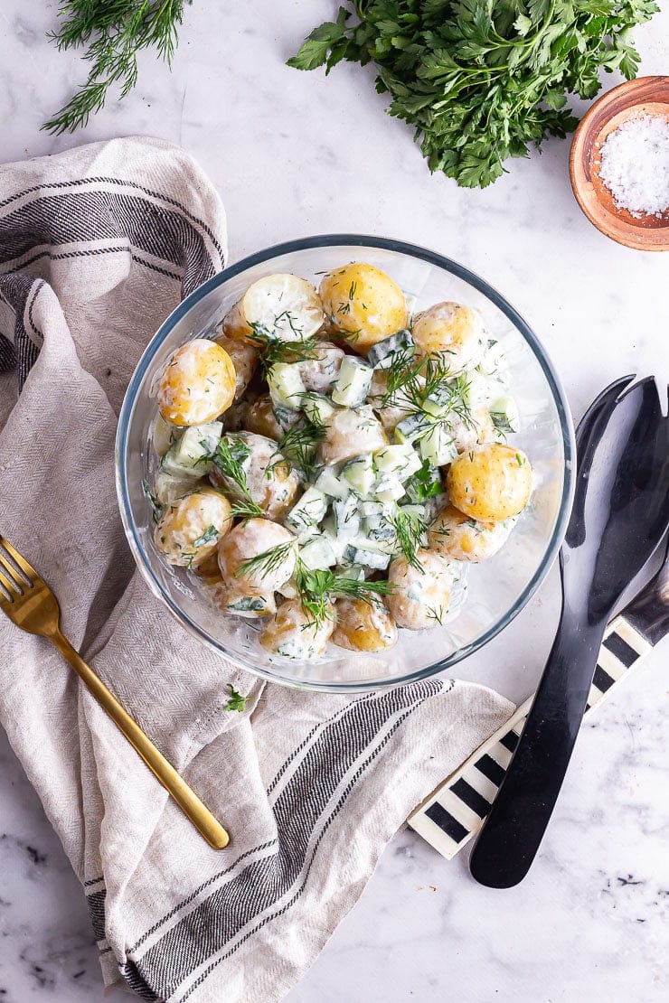 Overhead shot of healthy potato salad with herbs, salt and salad servers