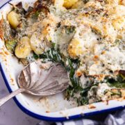 Spoon and salmon gnocchi bake in a white baking tin with checked cloth