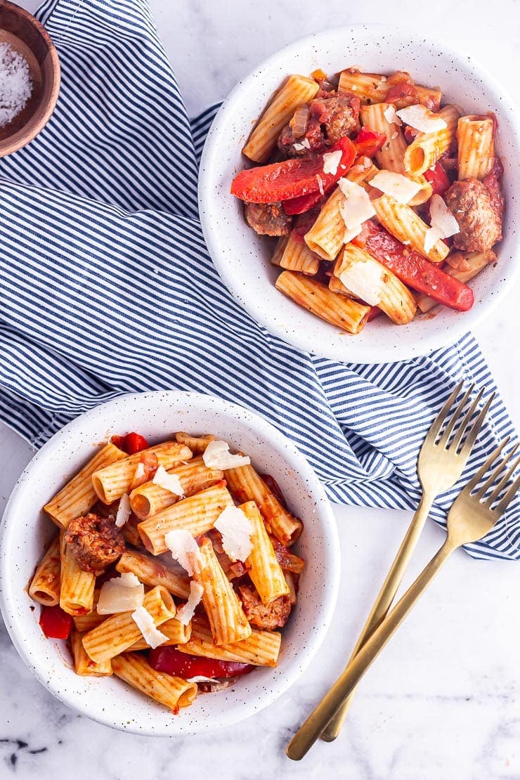 Overhead shot of two bowls of sausage pasta on a striped cloth