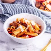 Close up of sausage pasta in a white speckled bowl on a marble surface