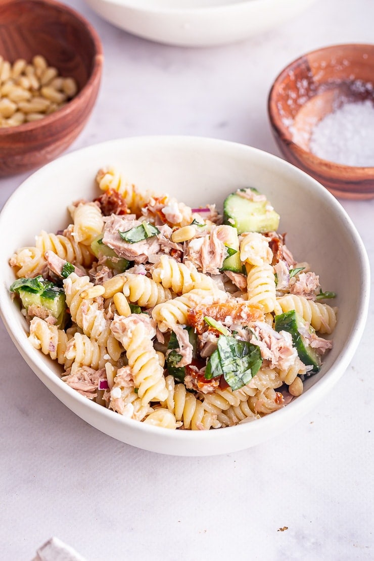 Side angle shot of tuna pasta salad in a white bowl on a marble surface