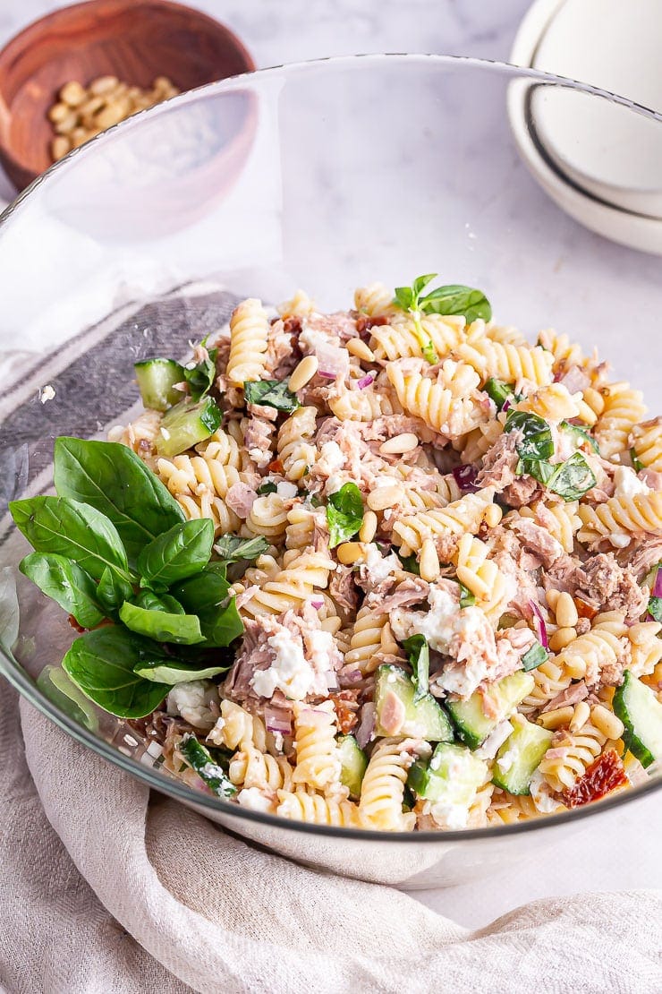 Glass bowl of tuna pasta salad with a cloth on a marble background